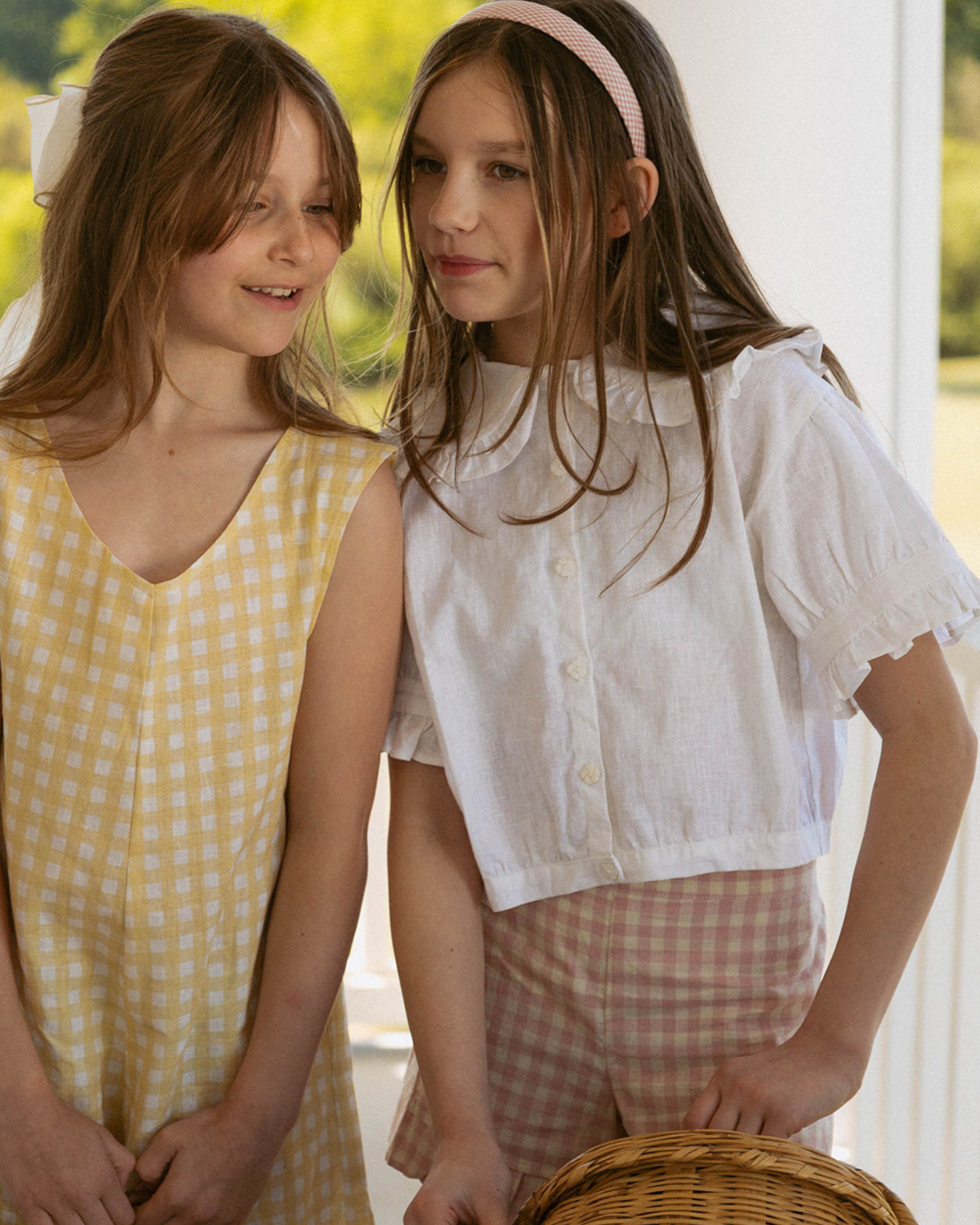 Two young girls standing next to each other outdoors, wearing light-colored clothing.