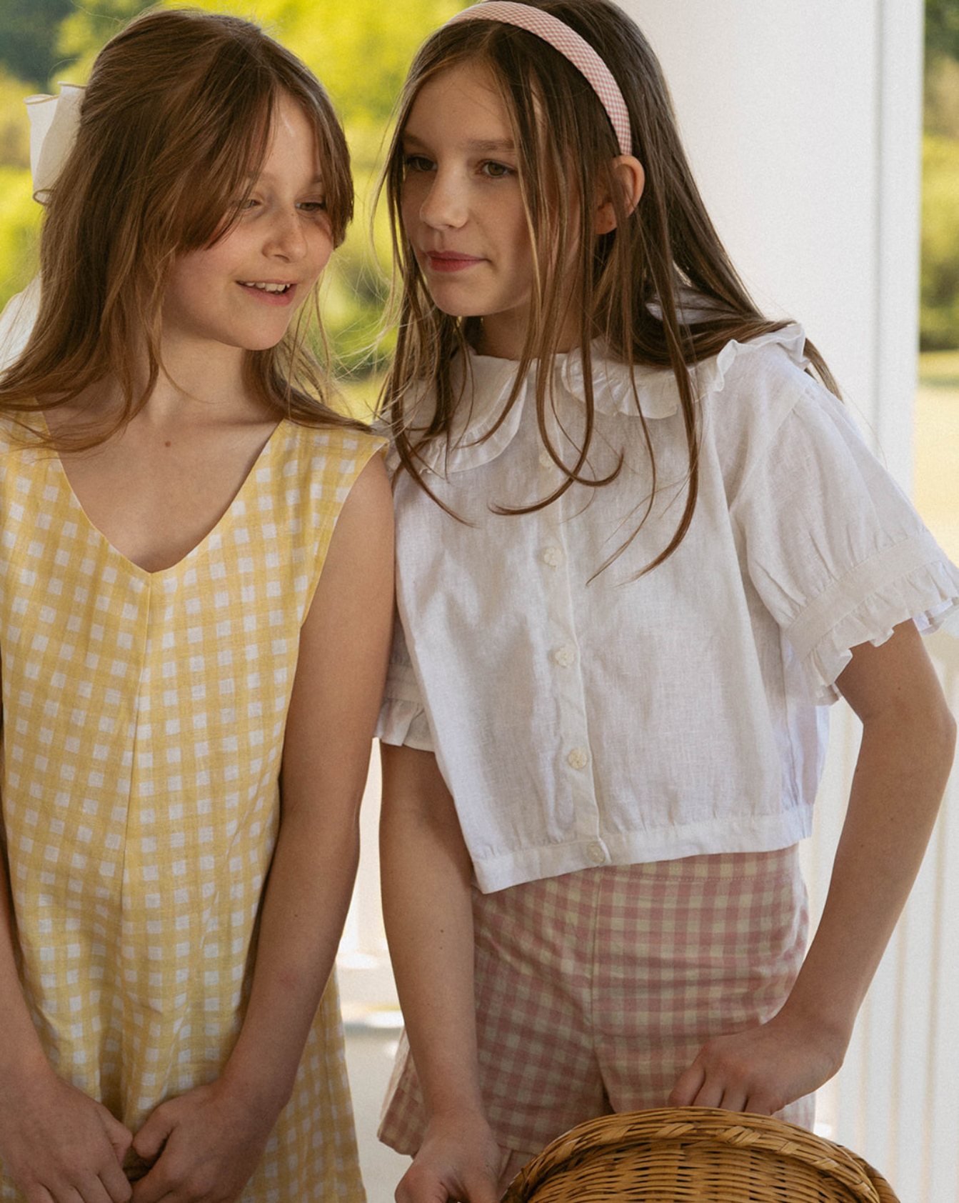 Two young girls standing next to each other outdoors, wearing light-colored clothing.