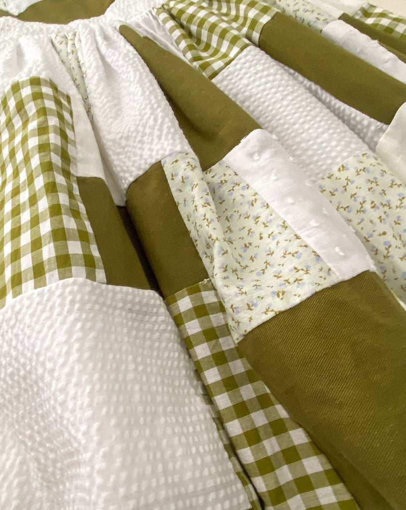 A close up image of the Mayday Patchwork dress, showing the range of textured and patterned fabrics, beautifully pieced together to form a unique green and white hued dress